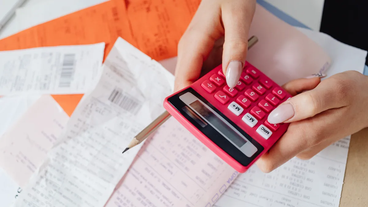 Mãos usando uma calculadora rosa para conferir recibos e contas