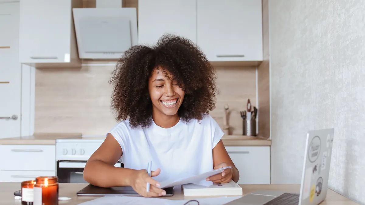 Mulher sorrindo enquanto revisa documentos ao lado do notebook