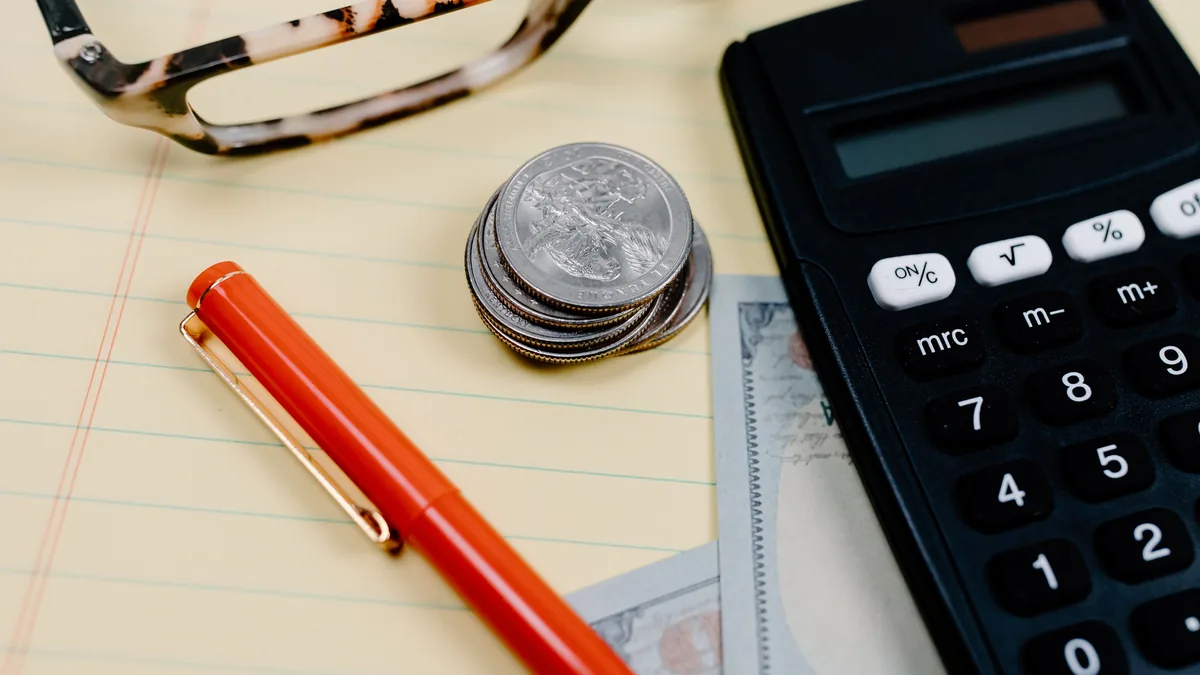 Calculadora, moedas e óculos sobre um caderno de contas